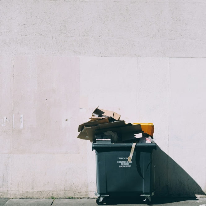 black plastic garbage bin with wheels beside wall