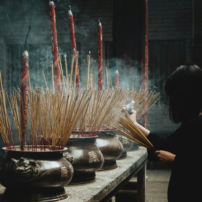 woman putting incense sticks on pot