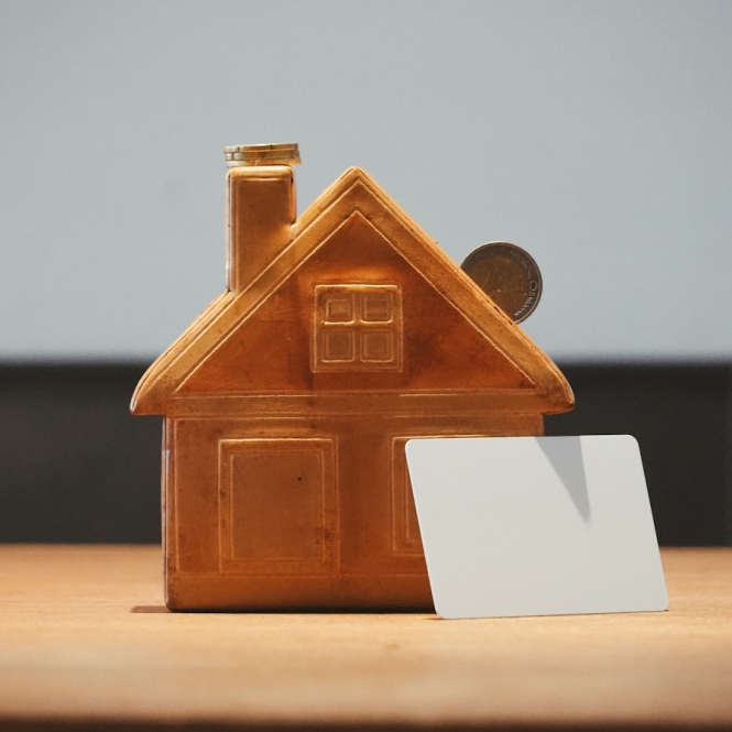 A small house bank with a coin and blank card.