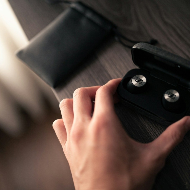 a person's hand holding a pair of black earbuds