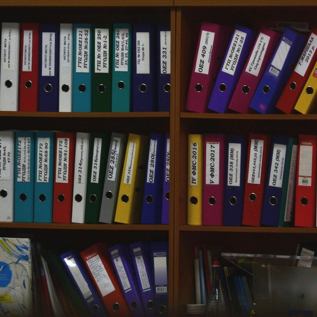 Rows of colorful ring binders organized on wooden shelves in an office
